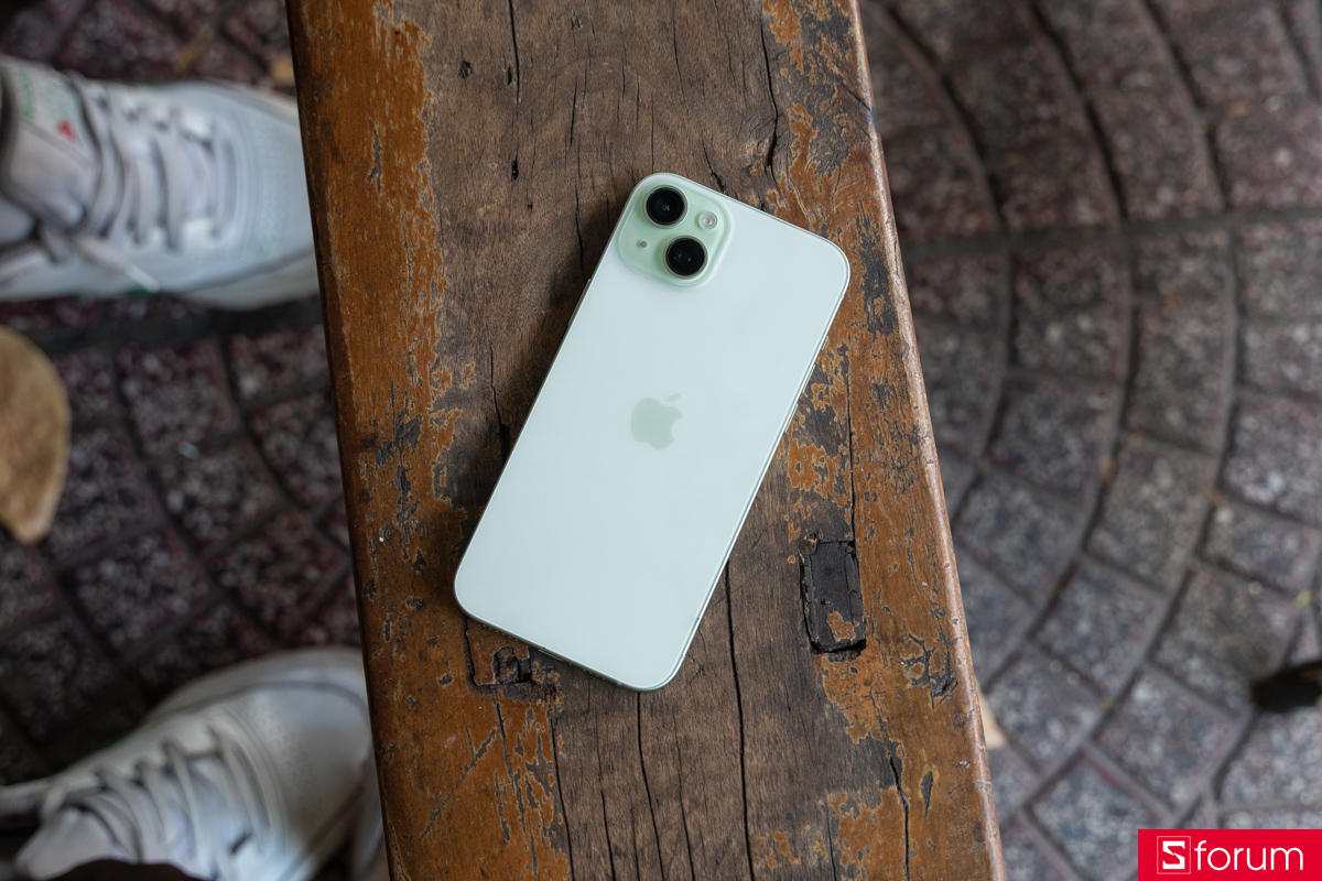 Mặt lưng kính nhám phối màu xanh lá nhẹ nhàng của iPhone 15 Plus đặt trên ghế gỗ