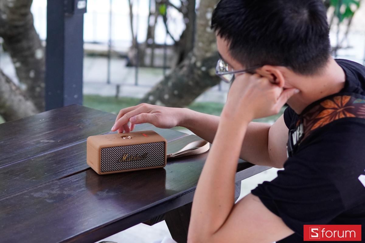 Người dùng chạm tay lên Marshall Emberton III trên bàn ngoài trời